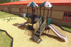 A red playground with stairs, two slides, two towers and sphere windows.